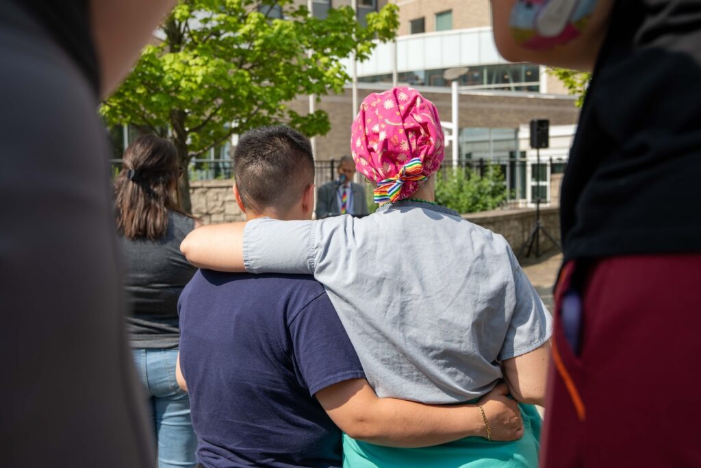 Two staff hugging while listening to speaker at pride month event
